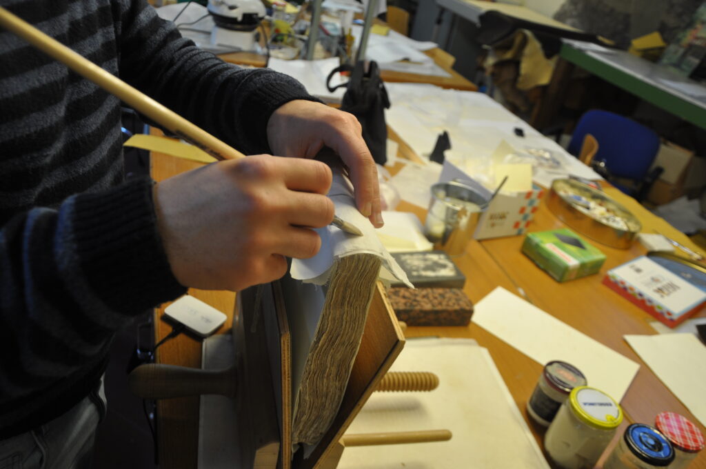 Lavorazione manuale della legatura del De re anatomica durante il restauro
